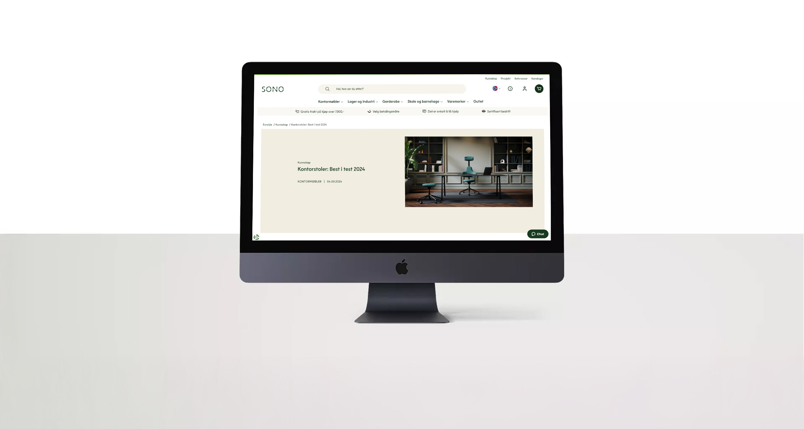En mørkegrå iMac på en hvit flate viser nettsiden til Sono med en artikkel om kontorstoler på skjermen mot lys bakgrunn.